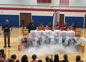 Teachers pouring liquid on dry ice for student audience in the gym