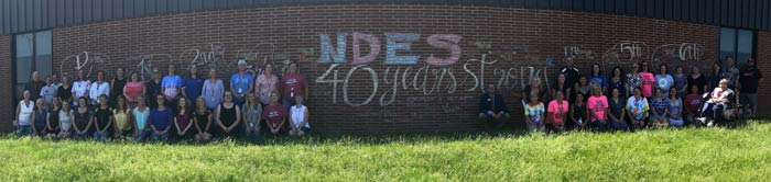 Staff in front of brick wall with NDES 40 Years Strong written on it